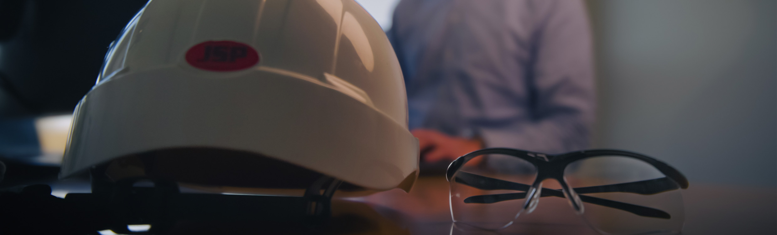 Construction helmet and protective glasses on the desk of the occupational health and safety manager that reads an occupational health and safety white paper. 